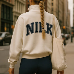 Back view of NILK Cream Dream Team quarter-zip sweatshirt with bold back logo, worn on city street, stylish pickleball apparel