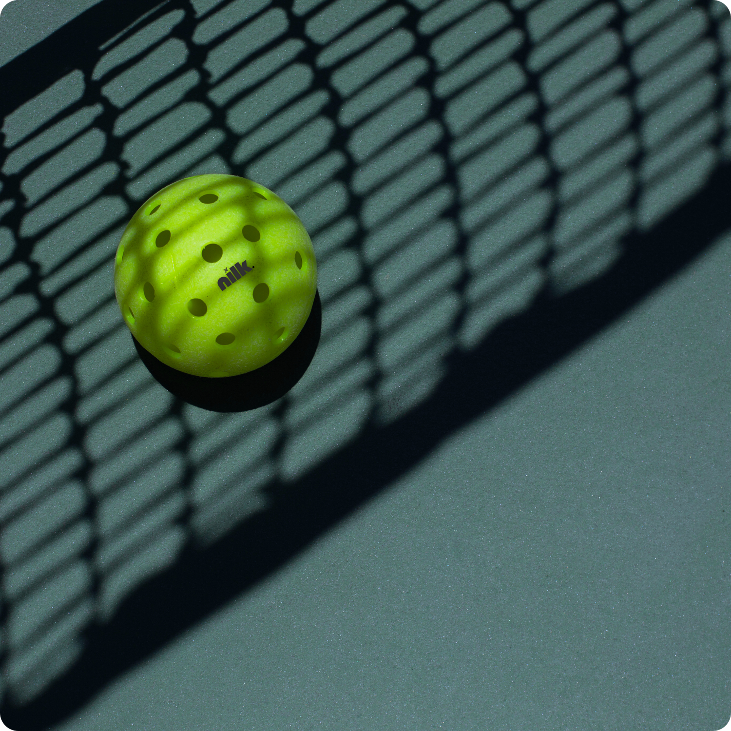 A bright green Nilk pickleball resting near the net, casting a shadow, illustrating faults and net rules in pickleball.